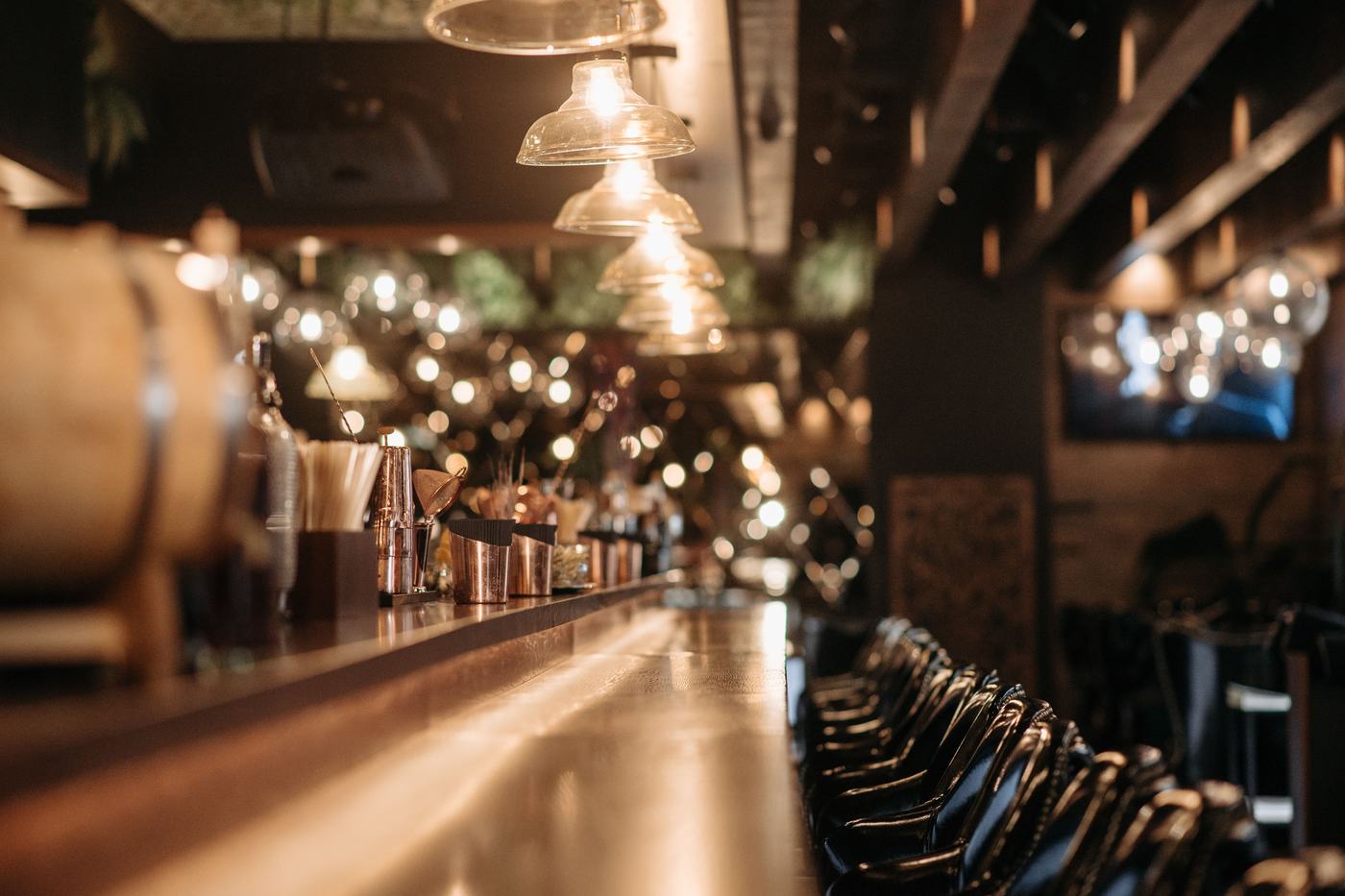 The bar at Emily&rsquo;s after dark: a long copper counter running away under a row of glass pendant lamps, shakers and jiggers set out at the near end.